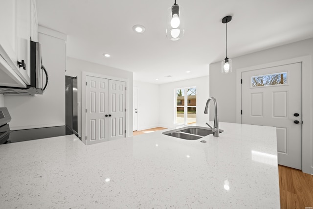 kitchen featuring a sink, white cabinetry, appliances with stainless steel finishes, light stone countertops, and decorative light fixtures