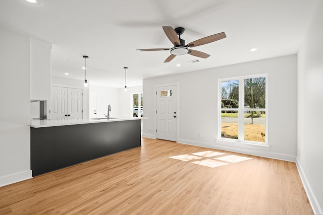 unfurnished living room with light wood finished floors, baseboards, a sink, and recessed lighting