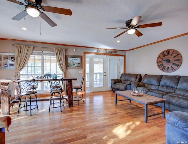 living room featuring light wood-style floors, crown molding, a ceiling fan, and a textured ceiling