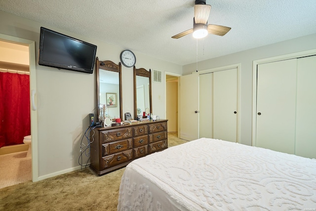bedroom featuring multiple closets, a textured ceiling, visible vents, light colored carpet, and ensuite bath