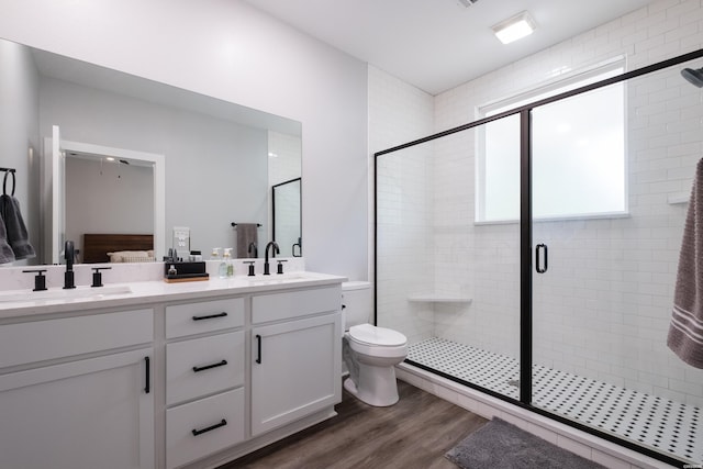 bathroom featuring double vanity, wood finished floors, a shower stall, and a sink
