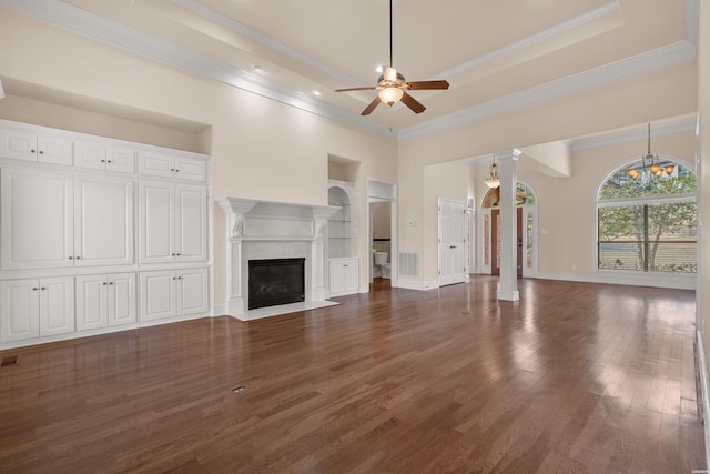 unfurnished living room featuring built in features, wood finished floors, a tray ceiling, a fireplace, and ceiling fan with notable chandelier