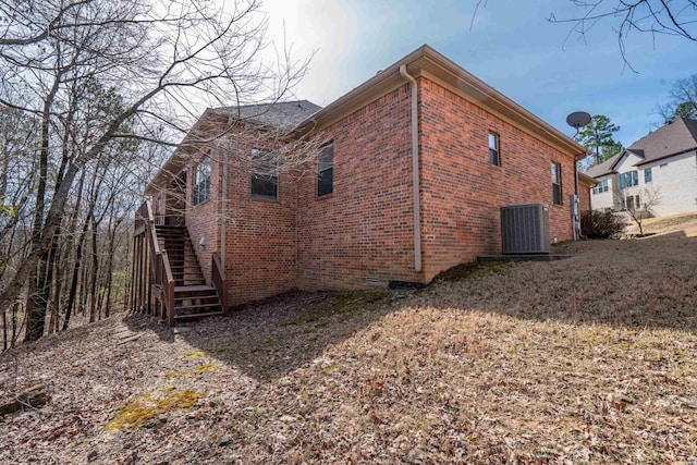 view of side of property featuring brick siding, crawl space, cooling unit, and stairway