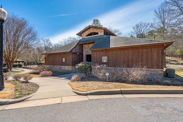 view of front of property featuring stone siding, central AC unit, and a shingled roof