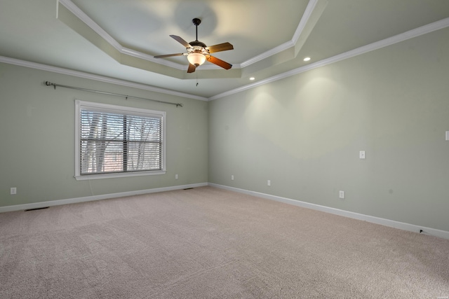 empty room featuring a raised ceiling, a ceiling fan, crown molding, baseboards, and light colored carpet