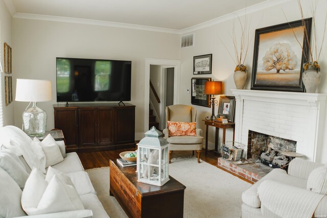 living area with a fireplace, visible vents, wood finished floors, and ornamental molding