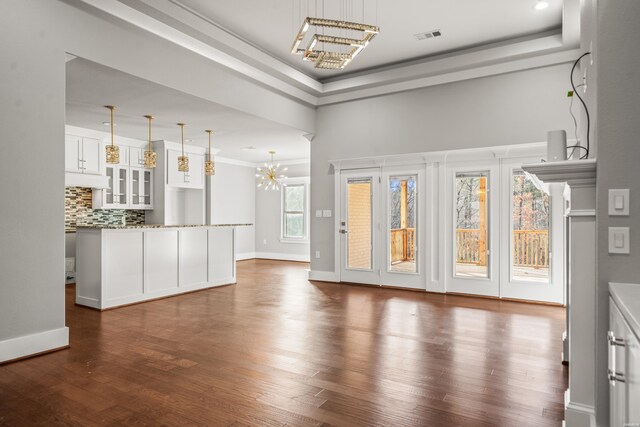 unfurnished living room featuring a raised ceiling, dark wood finished floors, visible vents, and a notable chandelier