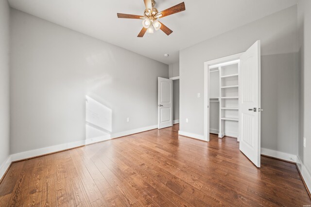 unfurnished bedroom featuring a walk in closet, a closet, a ceiling fan, wood finished floors, and baseboards