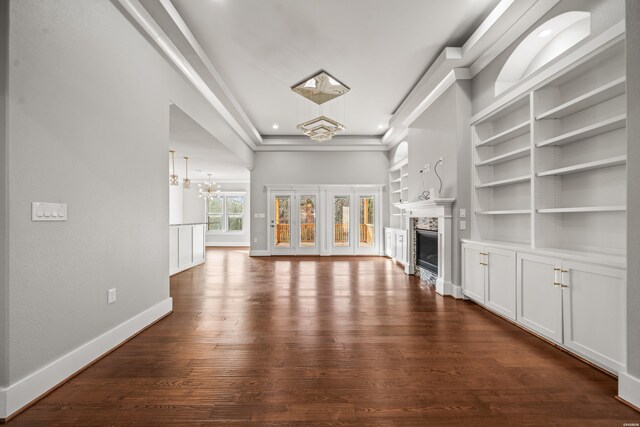 unfurnished living room with crown molding, a fireplace, an inviting chandelier, dark wood-type flooring, and baseboards