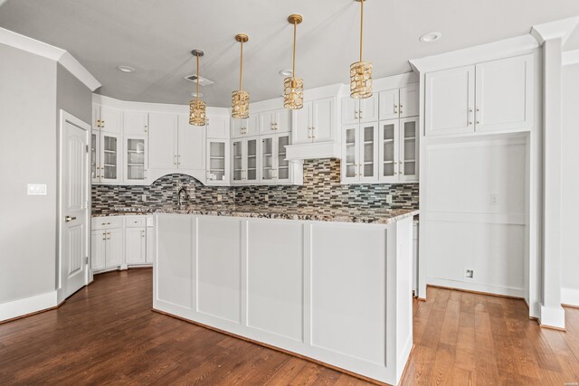 kitchen with hanging light fixtures, glass insert cabinets, dark wood-type flooring, white cabinets, and light stone countertops