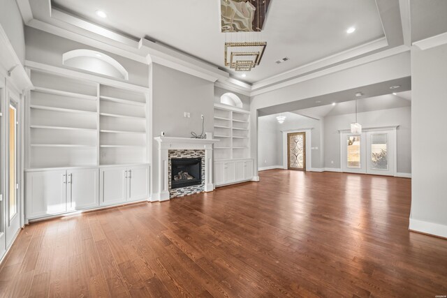 unfurnished living room featuring baseboards, wood finished floors, a tray ceiling, a stone fireplace, and built in shelves