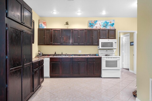 kitchen featuring white appliances, light countertops, a sink, and dark brown cabinetry