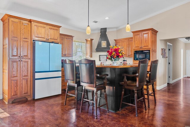 kitchen with black microwave, a breakfast bar area, freestanding refrigerator, decorative light fixtures, and custom range hood