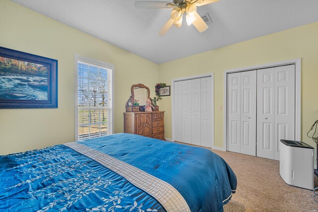 carpeted bedroom featuring a ceiling fan, a textured ceiling, visible vents, and two closets