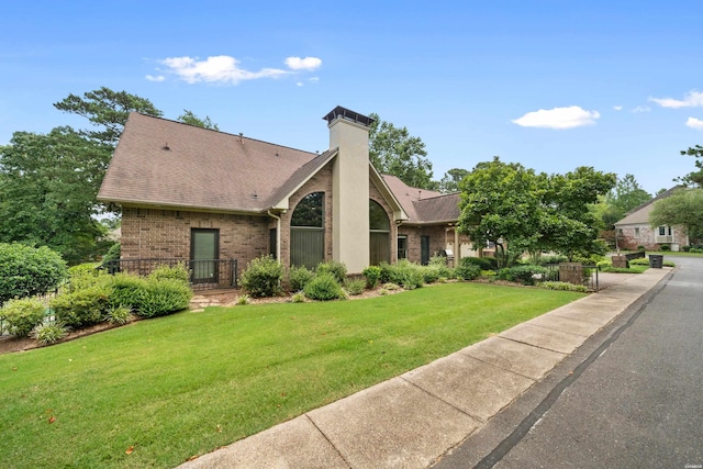 mid-century home with a shingled roof, a chimney, a front lawn, and brick siding