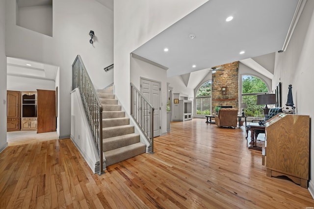 foyer with a ceiling fan, stairway, a high ceiling, light wood-type flooring, and a fireplace