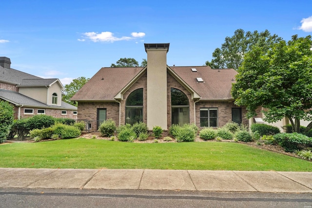 view of front of house with a chimney, brick siding, a front lawn, and a shingled roof