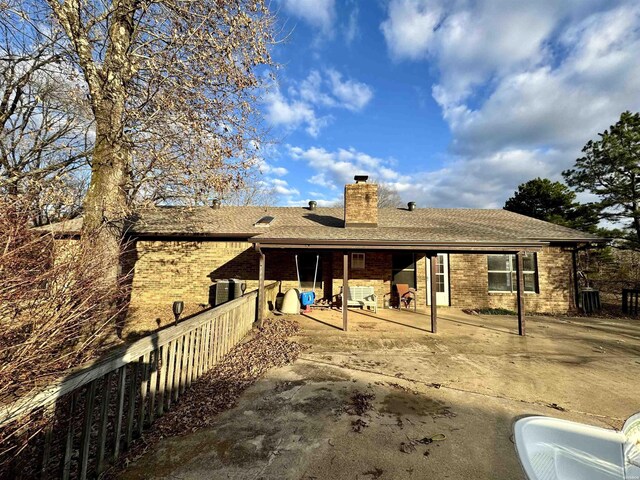 rear view of property with a patio, a chimney, roof with shingles, fence, and brick siding