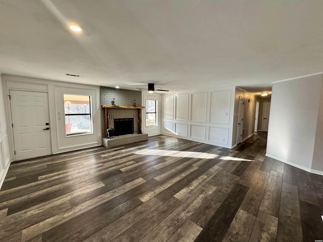 unfurnished living room with a fireplace, visible vents, a decorative wall, and dark wood-style flooring