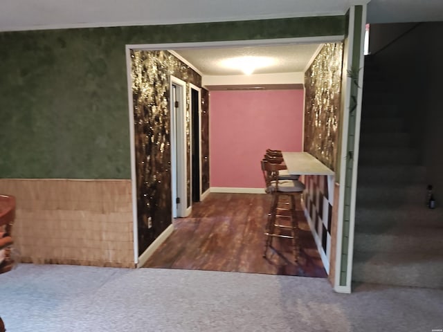 corridor with a wainscoted wall, dark colored carpet, and dark wood-style flooring