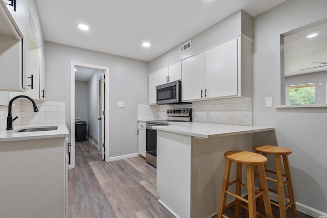 401 Buttrum Rd, Royal, AR 71968 - kitchen featuring stainless steel appliances, backsplash, white cabinets, light wood-style floors, and a kitchen bar
