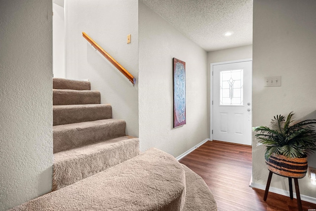 entrance foyer with dark wood-style flooring, a textured ceiling, baseboards, and stairs