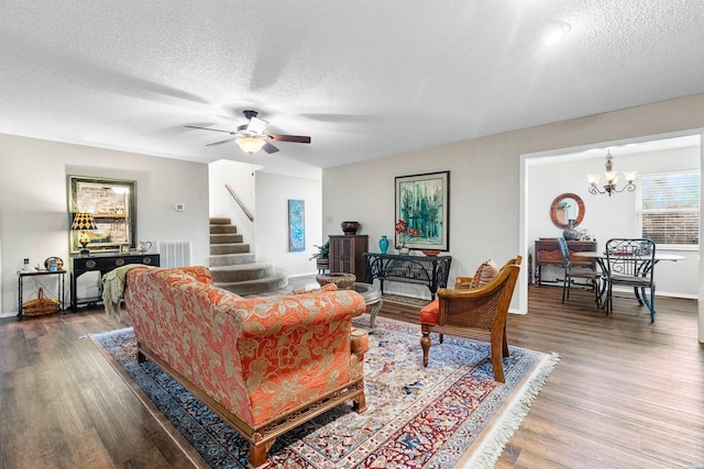 living area featuring ceiling fan with notable chandelier, wood finished floors, visible vents, and stairs