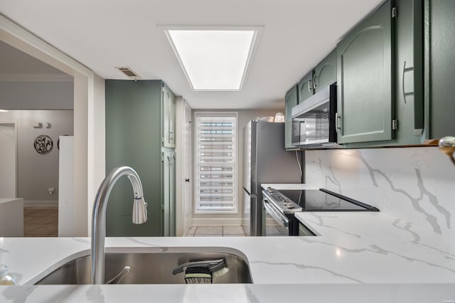 kitchen featuring light tile patterned floors, a sink, decorative backsplash, appliances with stainless steel finishes, and green cabinets