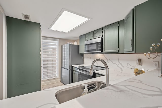 kitchen with light stone counters, visible vents, green cabinetry, appliances with stainless steel finishes, and tasteful backsplash