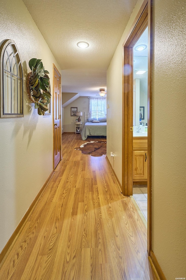 hall with light wood finished floors, vaulted ceiling, a sink, a textured ceiling, and baseboards