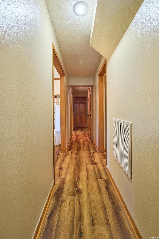 hall featuring visible vents, a textured wall, dark wood-type flooring, a textured ceiling, and baseboards