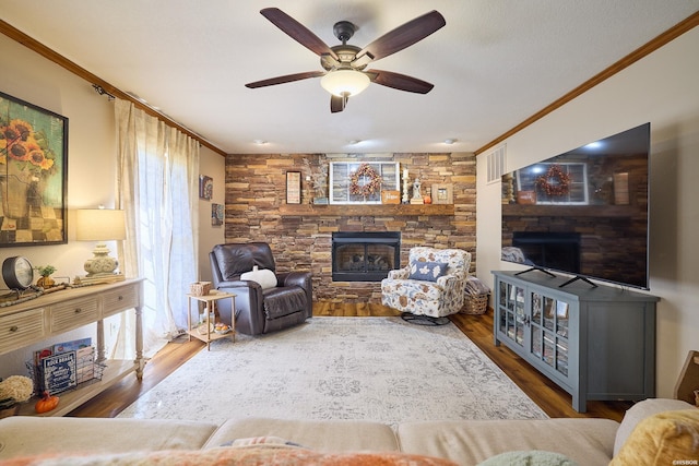 living area with ornamental molding, a stone fireplace, wood finished floors, and a ceiling fan