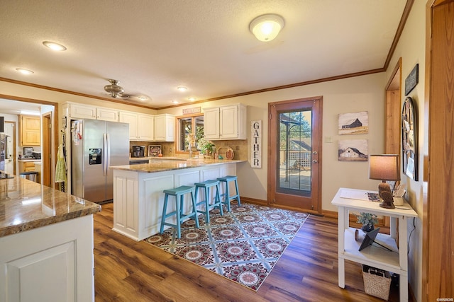 kitchen with a breakfast bar area, white cabinets, dark stone counters, a peninsula, and stainless steel fridge with ice dispenser