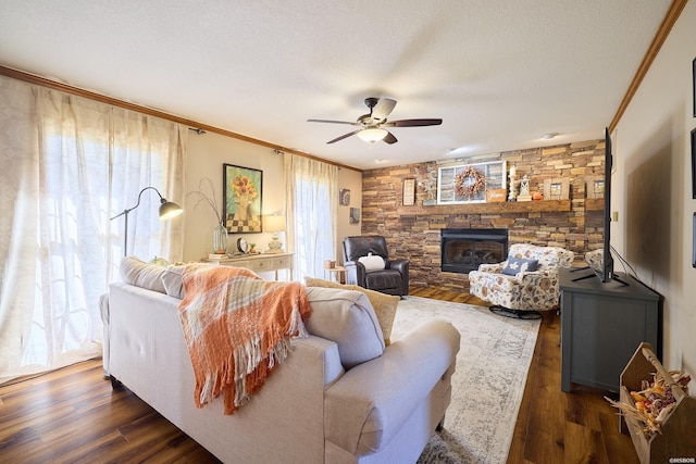 living area featuring ornamental molding, dark wood-style flooring, a stone fireplace, and a ceiling fan