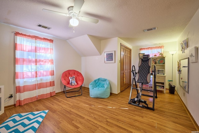 workout room featuring light wood-type flooring, baseboards, visible vents, and a textured ceiling