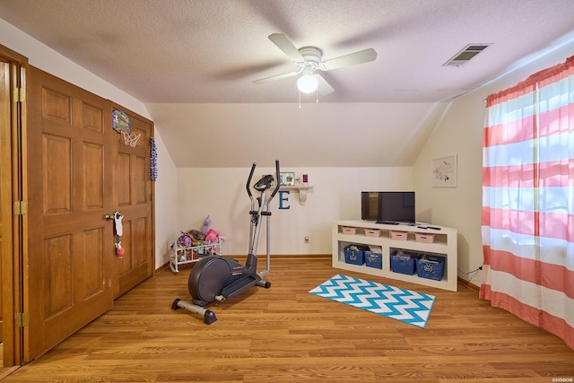 workout area featuring visible vents, vaulted ceiling, a textured ceiling, and light wood finished floors