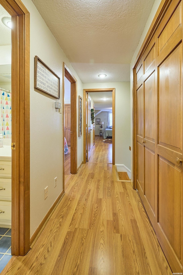 hall with a textured ceiling, light wood-type flooring, and baseboards