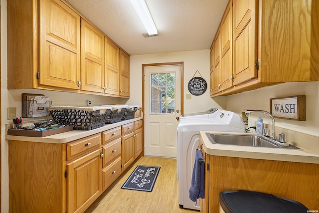 clothes washing area with a textured ceiling, a sink, light wood-type flooring, cabinet space, and washer and clothes dryer