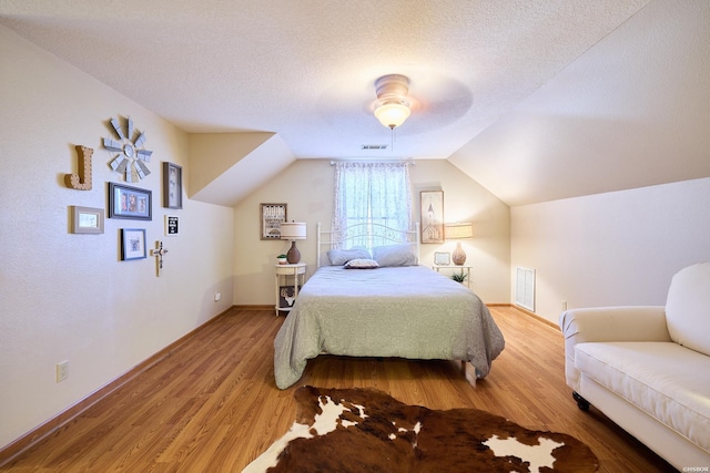 bedroom featuring a textured ceiling, wood finished floors, visible vents, and lofted ceiling