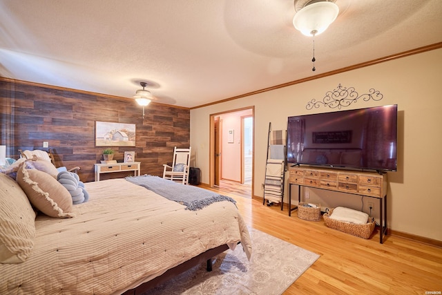 bedroom with baseboards, a ceiling fan, an accent wall, ornamental molding, and wood finished floors