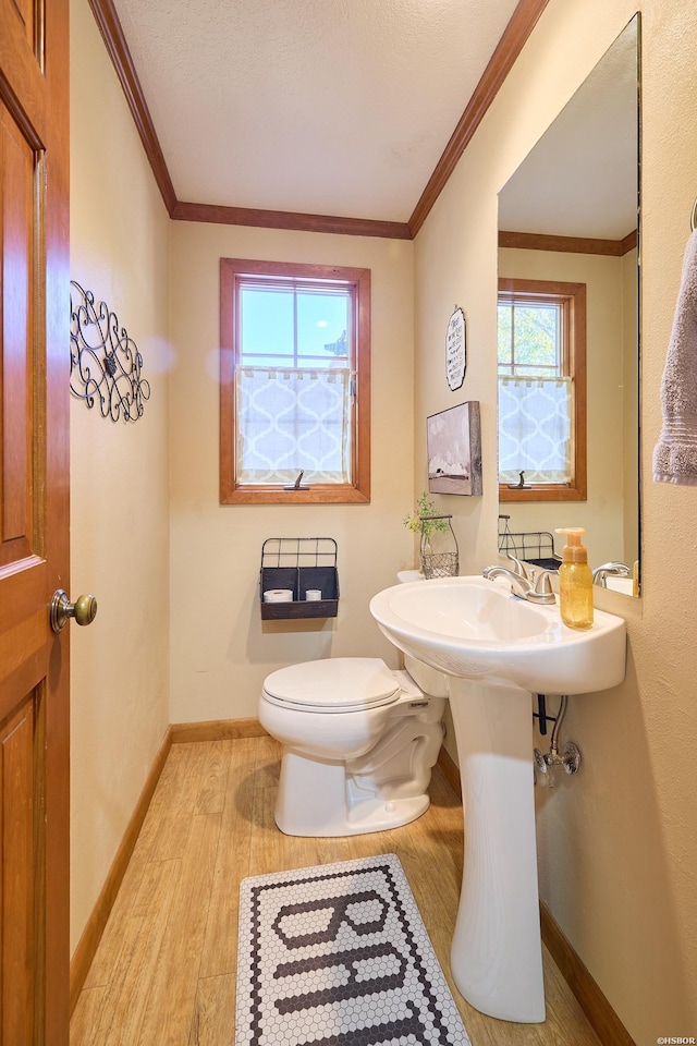 half bath featuring baseboards, wood finished floors, toilet, and crown molding