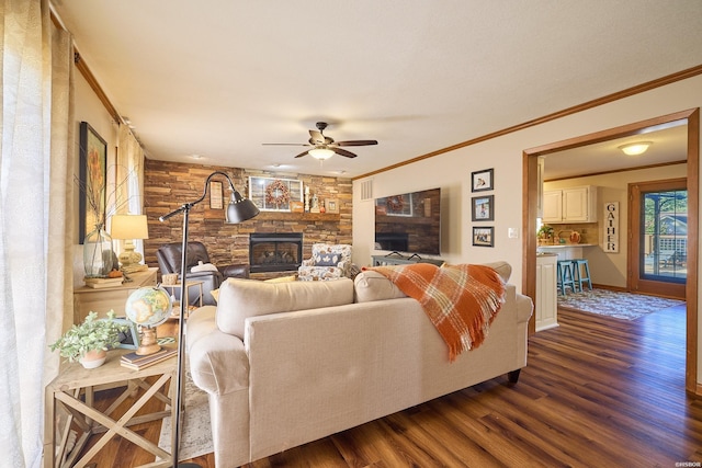 living room with ornamental molding, dark wood finished floors, a stone fireplace, and a ceiling fan