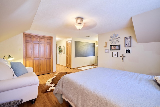 bedroom with lofted ceiling, light wood finished floors, a ceiling fan, and a closet