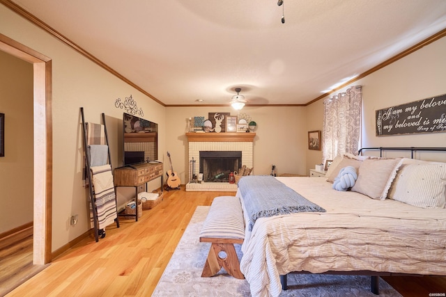 bedroom featuring ornamental molding, a brick fireplace, ceiling fan, wood finished floors, and baseboards