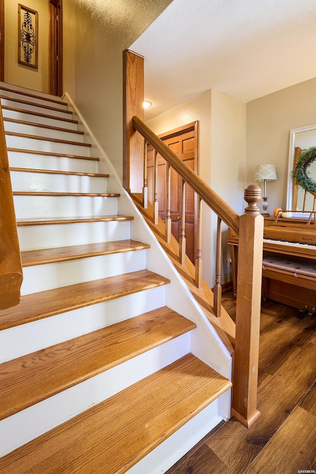 stairs with a textured ceiling and wood finished floors