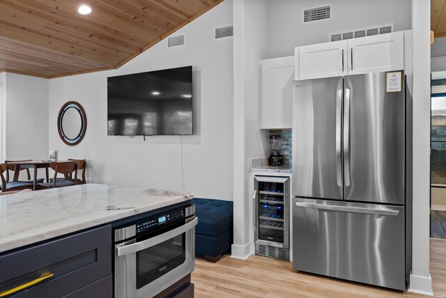 kitchen with light stone counters, beverage cooler, white cabinetry, light wood-type flooring, and freestanding refrigerator