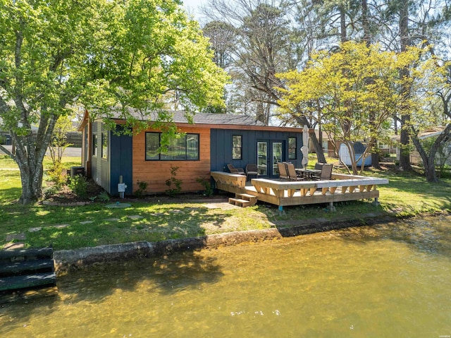 rear view of house with a deck with water view and a yard