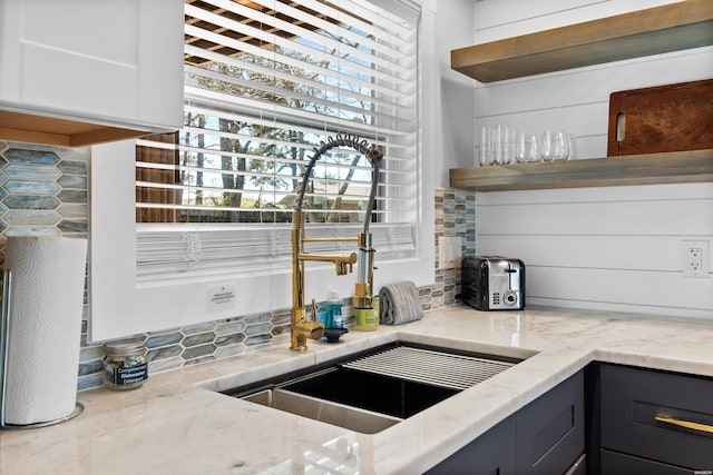 kitchen with light stone counters, open shelves, decorative backsplash, white cabinets, and a sink