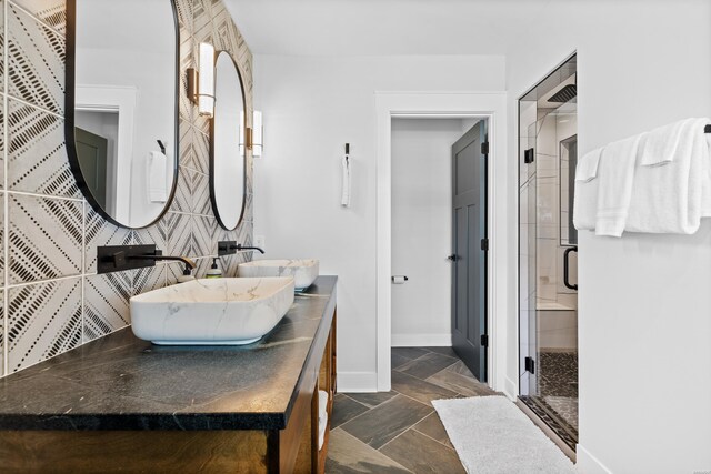 full bath featuring double vanity, a stall shower, baseboards, and a sink