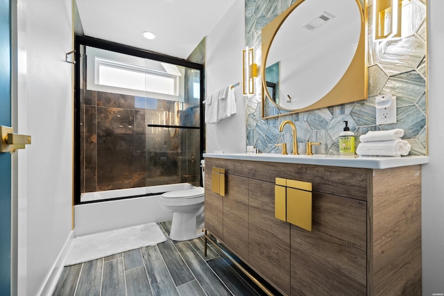 bathroom with toilet, visible vents, vanity, combined bath / shower with glass door, and wood tiled floor